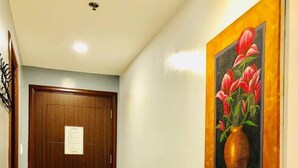 A hallway with a wooden door and a painting of flowers on the wall. - Umali Kayo at Megatower Residences 1 (Baguio)