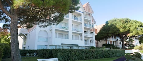Un edificio de varios pisos con balcones, un banco y una siega en primer plano.