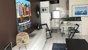 A modern kitchen with white cabinets, a dining area with a black table and chairs, and a large painting of a colorful boat on the wall. - Apartment with direct beach access (parking, Wi-Fi, near downtown)—check out the reviews! (Arcachon)