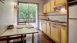 A kitchen with a dining table, chairs, a refrigerator, and a window with a view of greenery outside. - N&J - MARIN DEBUSSY - Hyper center (Niza)