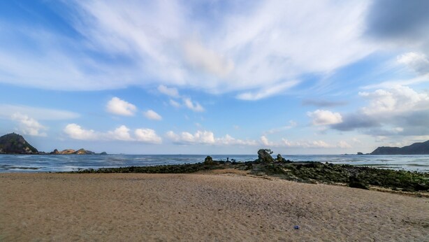 Una playa con un promontorio rocoso y mar tranquilo.