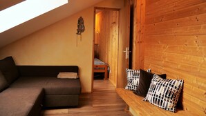 A cozy room with a sloped ceiling, a wooden bench with patterned cushions, a sofa, and a small bed with a checkered blanket.