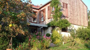 A rustic wooden house with a balcony, surrounded by a garden with various plants and flowers.
