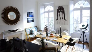 Comedor con una mesa de madera dispuesta para cuatro comensales, sillas blancas, un espejo grande y un cuadro en la pared.