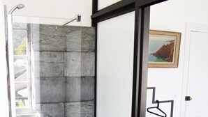 Un baño moderno con cabina de ducha de vidrio, una puerta blanca y una cama con colcha blanca.