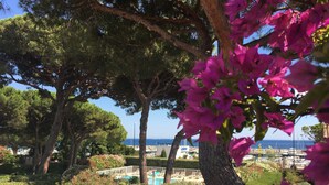Area piscina con lettini, circondata da alberi e siepi, con vista sul mare e imbarcazioni sullo sfondo.