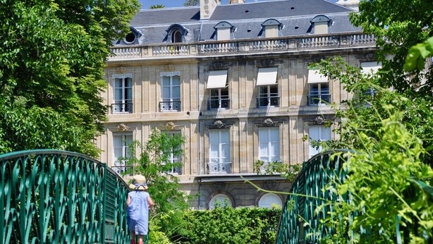 Un edificio histórico con fachada simétrica, ventanas grandes y un puente de hierro verde al frente.