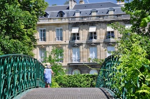 Un edificio histórico con fachada simétrica, ventanas grandes y un puente de hierro verde al frente.