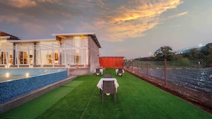 A hotel with a swimming pool, outdoor seating, and a view of the sunset. - Treebo Winter Town Venna Lake (Mahabaleshwar)