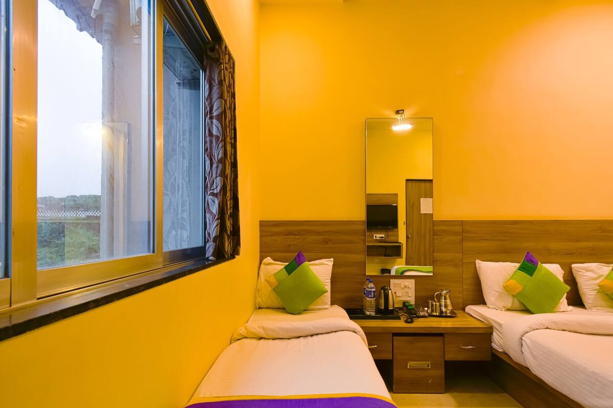 A hotel room with two beds, a wooden headboard, a bedside table with a mirror, a TV, and a window with curtains.