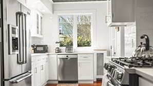 A modern kitchen with stainless steel appliances, white cabinetry, a dishwasher, and a window with a view of greenery.