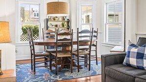 A dining area with a wooden table and chairs, a hanging lamp, and a blue patterned rug.