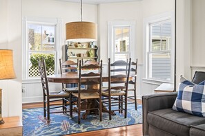 A dining area with a wooden table and chairs, a hanging lamp, and a blue patterned rug.