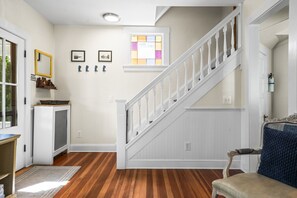 A hallway with a wooden floor, a white staircase, and a door with a blue chair.