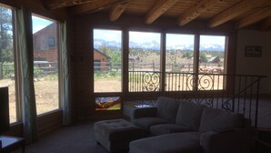 Ein gemütliches Wohnzimmer mit einer Eckcouch, großen Fenstern mit Bergblick und einer Holzbalkendecke.