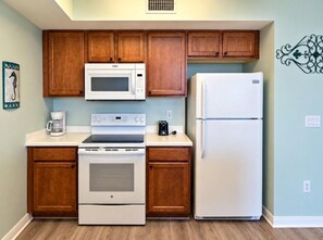 A kitchen with wooden cabinets, a microwave, a refrigerator, an oven, and a coffee maker.