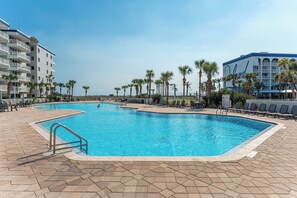 Una gran piscina al aire libre con palmeras y sillas de descanso, rodeada de edificios.