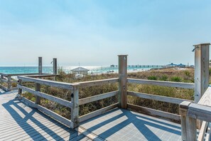 A wooden boardwalk leading to a beach with a pier in the background.