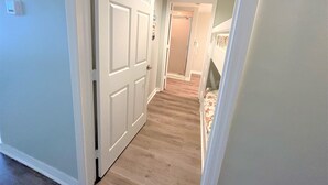 Un couloir avec une porte blanche, un sol recouvert de moquette et une chambre avec un lit superposé.
