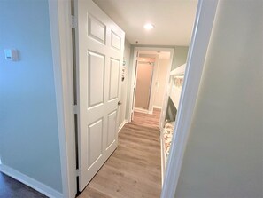 Um corredor com porta branca, chão coberto de carpete e um quarto com beliche.