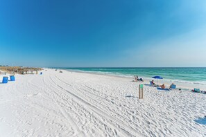 A beach with white sand, clear blue water, and a wooden pier.