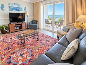 A living room with a large flat-screen TV, a sofa, a coffee table, and a colorful rug.