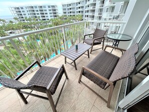 Varanda com móveis de vime, mesa de vidro e vista para uma piscina e edifícios.