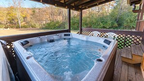 Un jacuzzi bajo una pérgola de madera con vistas a árboles y un área de picnic al fondo.