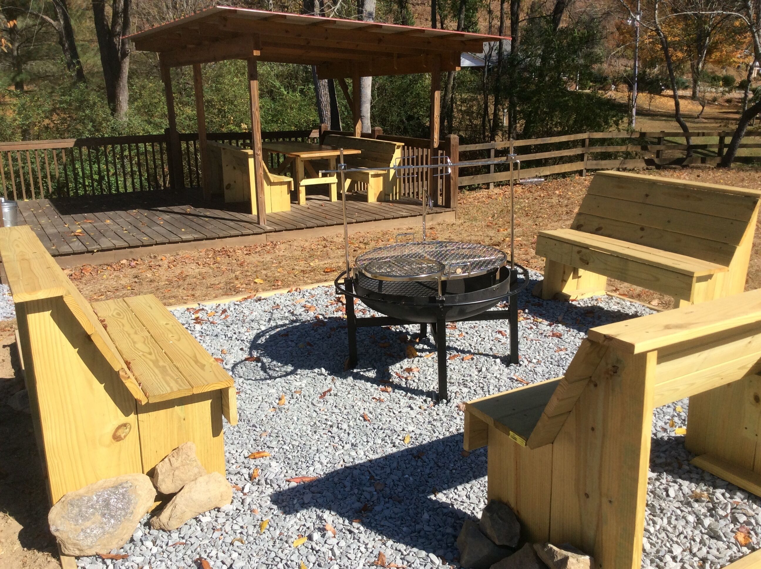 Un espace extérieur aménagé en bois, avec un foyer, des bancs, ainsi qu’une table et des chaises sous une pergola.