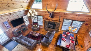 Interior de una cabaña con chimenea, asientos de cuero, una mesa de comedor lista para cuatro comensales y una cabeza de ciervo decorativa.