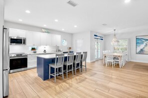 A modern kitchen with white cabinets, a central island with bar stools, and a dining area with a chandelier.