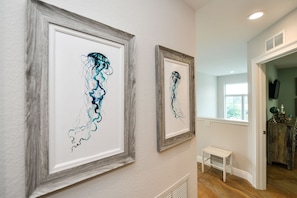 A hallway with two framed artworks on the wall, a small white bench, and a door leading to another room.