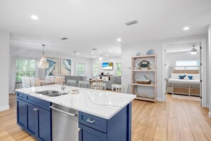 A spacious kitchen with a marble island, blue cabinets, and a dining area with a view of the beach.