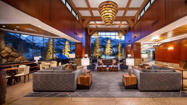 Un hall d’entrée spacieux avec un grand espace salon, un mur en pierre offrant une vue sur la montagne et un lustre moderne.