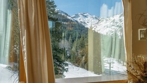 A window view of a snow-covered mountain landscape with a forested area and a ski lift in the background. - Largest 2BR Great Room at Everline - Sleeps 8  - End Unit (Olympic Valley)
