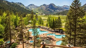 Un complexe hôtelier doté de plusieurs piscines entourées d’arbres, avec un terrain de golf en arrière-plan et des montagnes à l’horizon.