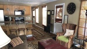 Ein Wohnzimmer mit Sofa, Hocker, Korbstuhl und einem Essbereich mit Stühlen und Tisch.