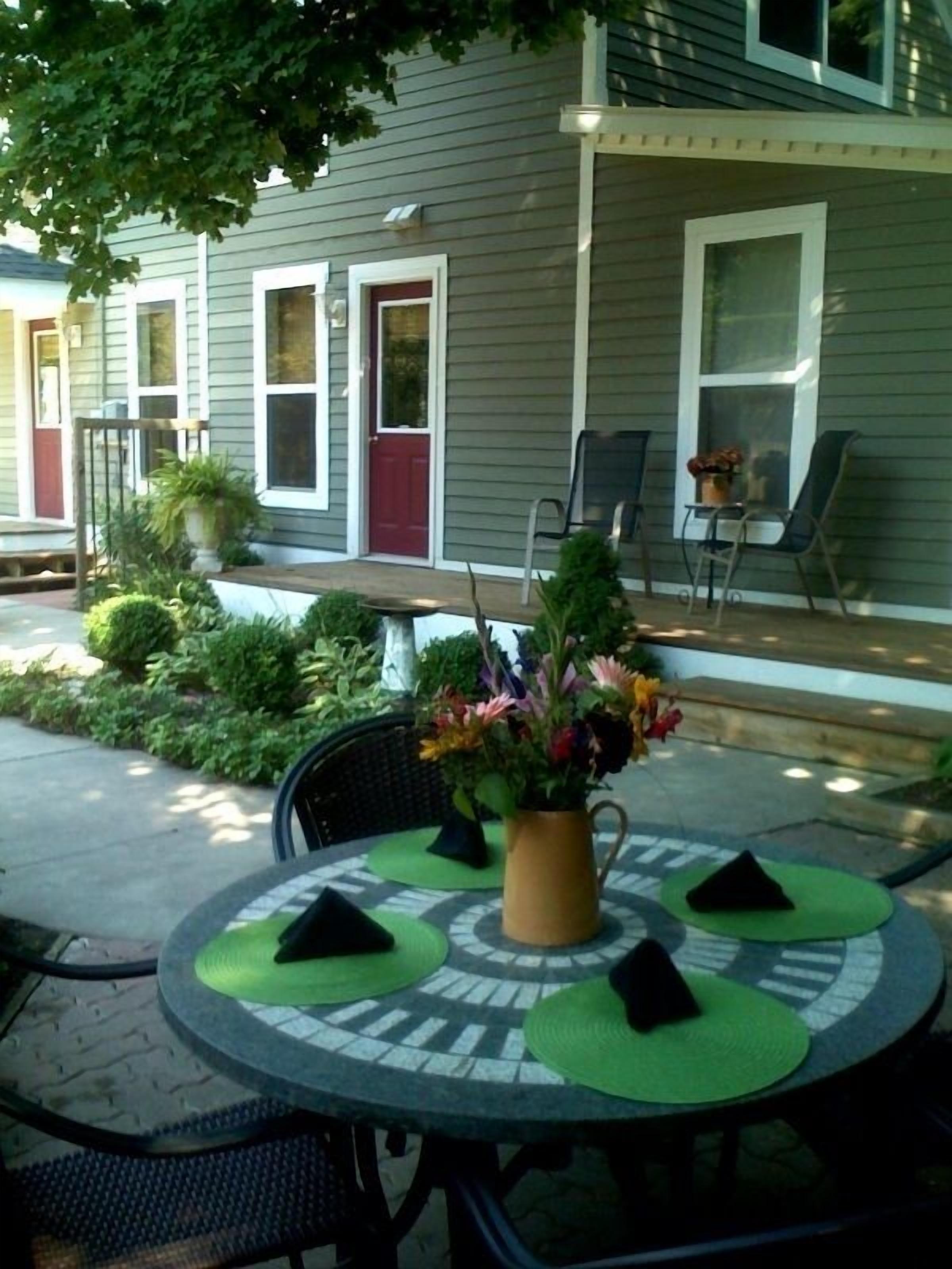 Une terrasse avec une table ronde, des sets de table verts et une plante en pot.