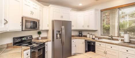 A kitchen with white cabinets, stainless steel appliances, a tiled floor, and a window with blinds.