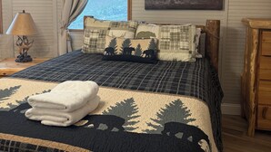 Un dormitorio con cama, ventana con cortinas, un cuadro en la pared y una lámpara en la mesita de noche.