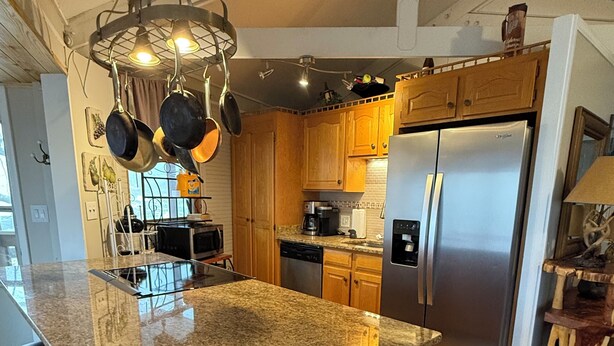 Una cocina con una isla grande de granito, electrodomésticos de acero inoxidable, armarios de madera y ollas colgantes.