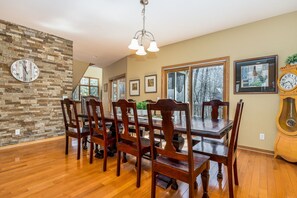 Une salle à manger avec une table et des chaises en bois, un mur en pierre et une grande fenêtre.