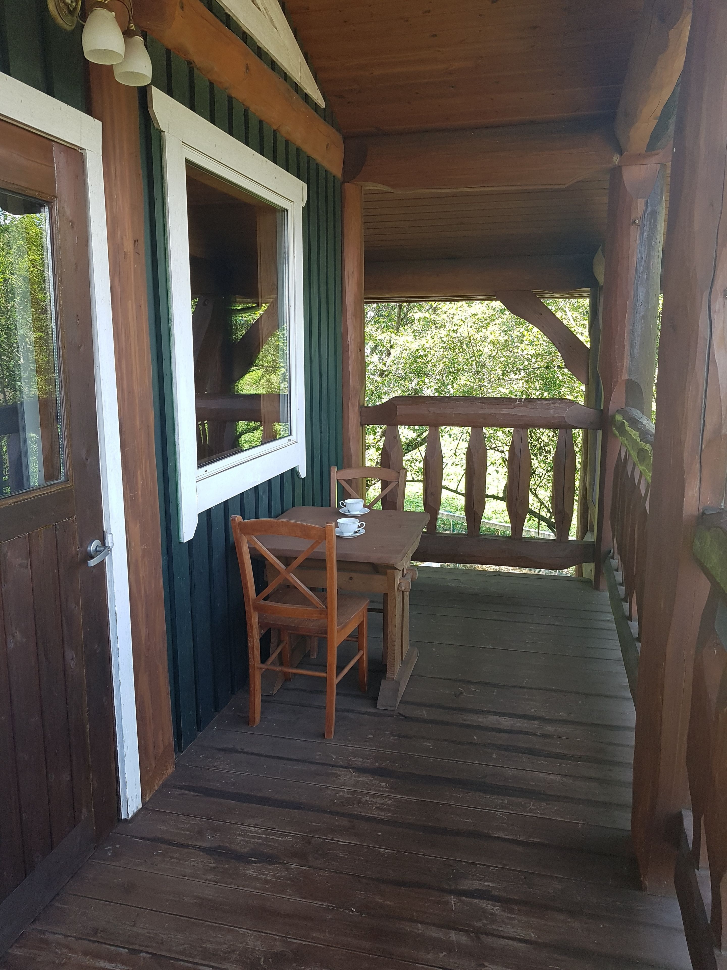 A wooden porch with a table and chair, a window, and a view of trees.