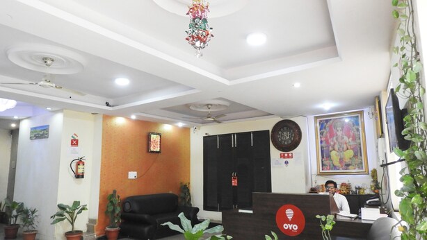 A reception area with a desk, chairs, potted plants, and a wall-mounted clock. - JKM Palace (New Delhi)