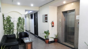 A reception area with a black leather sofa, a glass-top table, potted plants, and an elevator. - JKM Palace (New Delhi)