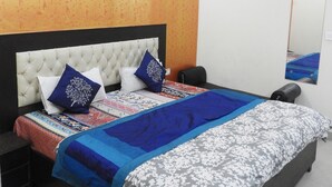 A modern bedroom with a tufted headboard, a patterned bedspread, and a large mirror on the wall. - JKM Palace (New Delhi)