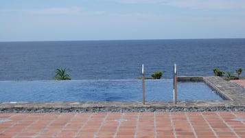 A pool with a view of the ocean, surrounded by a tiled patio.