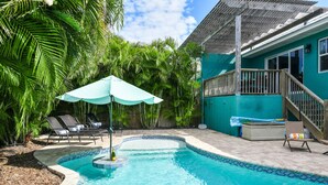 A swimming pool with lounge chairs and an umbrella, surrounded by lush greenery and a wooden deck. - Caribbean Reef! Cozy Pool Home Near Gulf! (Holmes Beach)