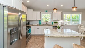 A modern kitchen with white cabinets, a stainless steel refrigerator, and pendant lighting. - Caribbean Reef! Cozy Pool Home Near Gulf! (Holmes Beach)