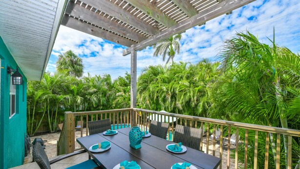 A covered outdoor dining area with a wooden pergola, a pool, and lush tropical vegetation. - Caribbean Reef! Cozy Pool Home Near Gulf! (Holmes Beach)